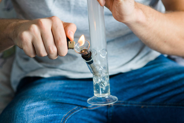 man smokes using Bong and medical marijuana, cannabis thc flower Sativa and Indica Close up on a black background. lifestyle Concepts the legalization of marijuana in the world and the - 写真・画像