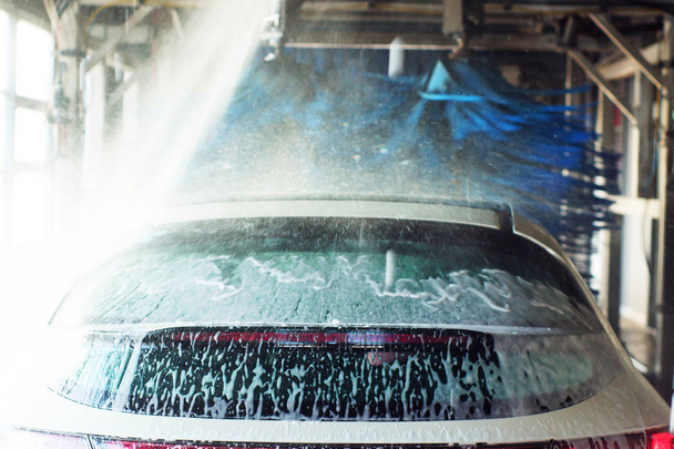 Car wash, zwarte auto in automatische Autowassen, roterende borstel van rood en blauw. Wassen voertuig. - Foto, afbeelding