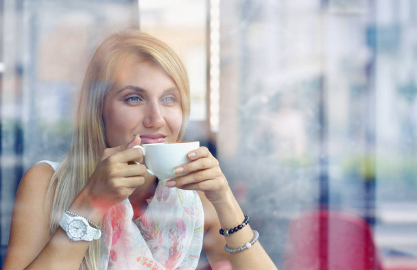 Retrato de uma menina pensativa bebendo café e olhando ao ar livre através de uma janela
 - Foto, Imagem