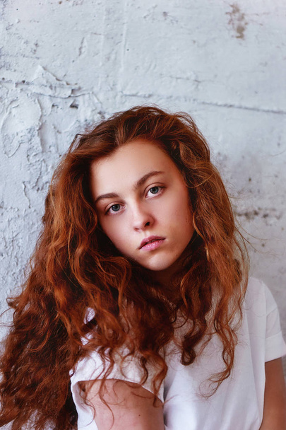 Model tests.Beautiful redhead girl with curly hair. Natural color. Krupneishego portrait on a background of light brick wall - Fotoğraf, Görsel