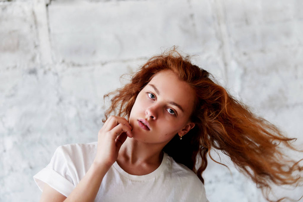 Model tests. Beautiful redhead girl with curly hair. Natural color. Dancing and moving on the background of light brick wall. Dynamics - Φωτογραφία, εικόνα