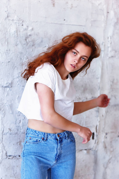 Model tests. Beautiful redhead girl with curly hair. Natural color. Dancing and moving on the background of light brick wall. Dynamics - Valokuva, kuva