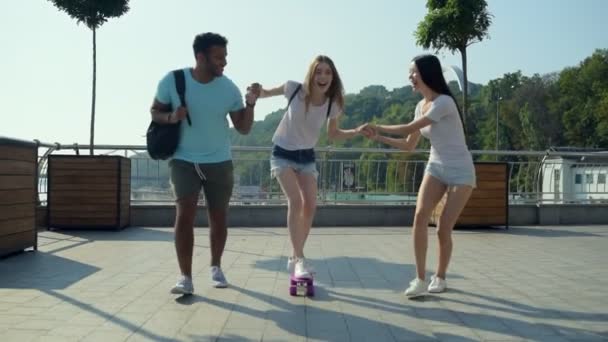 Positive girl learning skateboarding with friends - Footage, Video