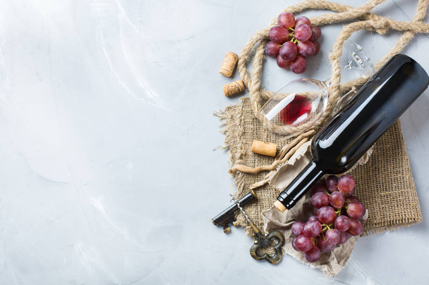 Бутылка, штопор, бокал красного вина, виноград на столе
 - Фото, изображение