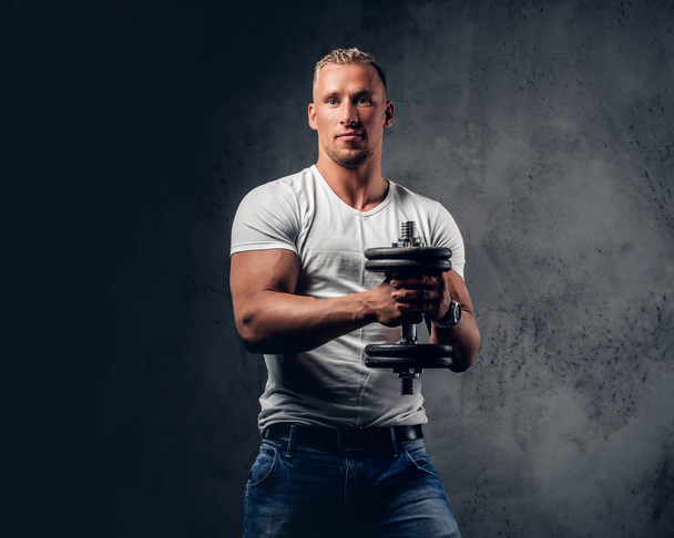 Handsome muscular male holds dumbbell - Photo, image
