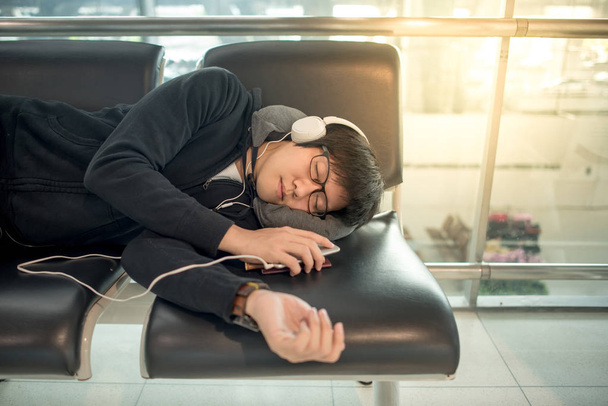 Young Asian man sleeping on bench in airport terminal - 写真・画像