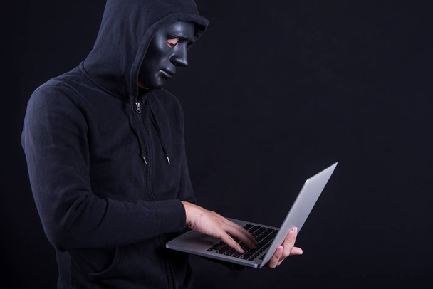 Mannelijke hacker met zwart masker uitvoering van laptop - Foto, afbeelding