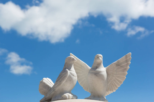 Два білих голуби з мармуру на тлі блакитного неба з хмарами
 - Фото, зображення