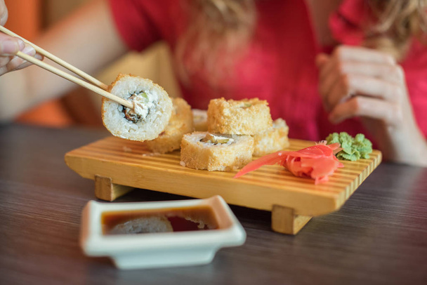 Dziewczyna jedzenia utrzymuje japoński jedzenie sushi rolki z chopsti drewniane - Zdjęcie, obraz