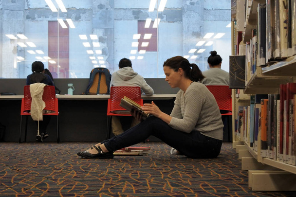 Female student reading a book in a library - Foto, Imagen
