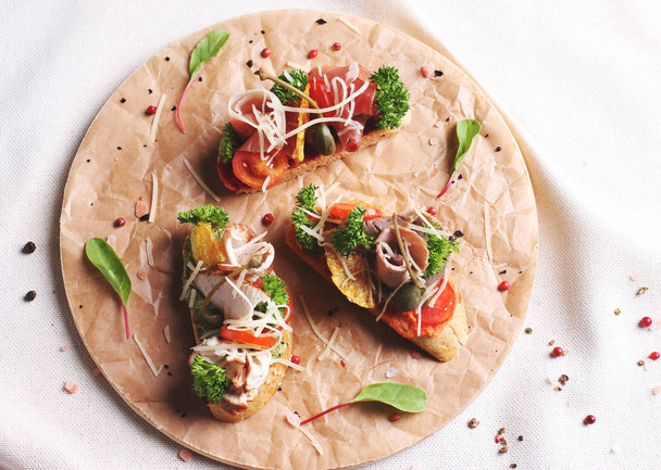 Bruschetta-Sandwich mit Schinken, Kräutern und Tomaten auf rundem Brett  - Foto, Bild
