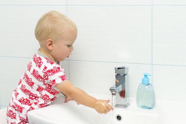 Close-up portrait of adorable white Caucasian boy toddler one year old washing hands in bathroom and looking surprised excited, playing with water - Photo, Image