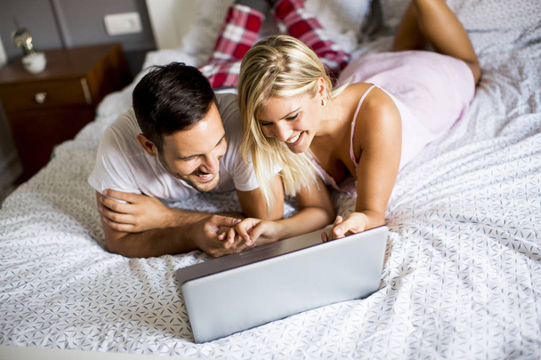 Amoureux intimes en utilisant un ordinateur portable couché sur le lit
 - Photo, image