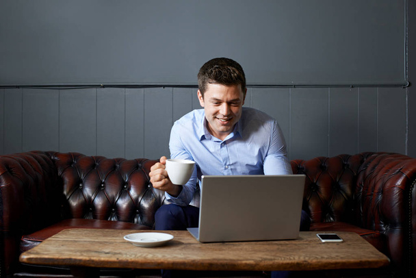 Businessman Drinking Coffee Whilst Working On Laptop In Internet - Фото, изображение