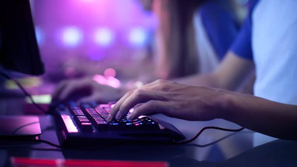 Close-up On Gamer's Hands on a keyboard, Actively Pushing Buttons, Playing MMO Games Online. Background is Lit with Neon Lights. - Fotó, kép