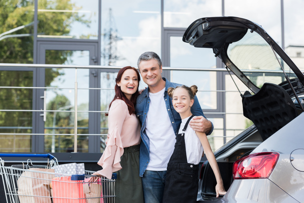 family with shopping cart next to car - Foto, Bild