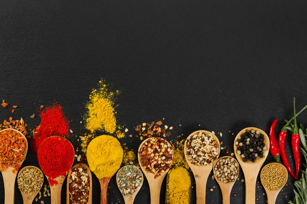 Assortment of natural spices on vintage spoons on dark slate