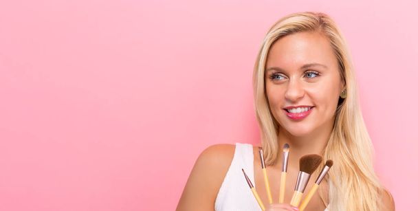 Beautiful young woman holding makeup brushes - Photo, image