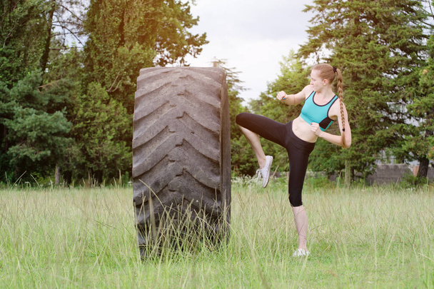 Girl in sports clothes is hitting the tire with her knee. street workout - Photo, Image