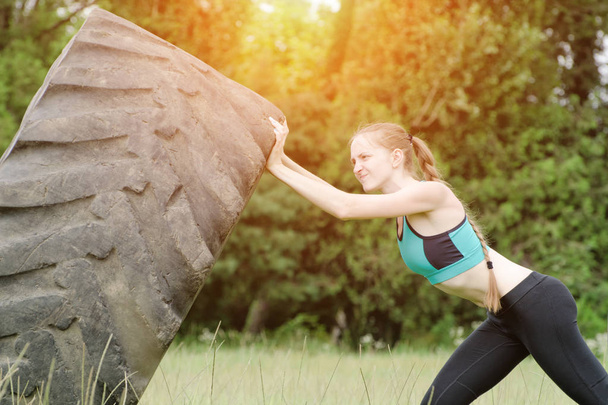 Girl in sportswear raises tire. Street workout. - Фото, изображение