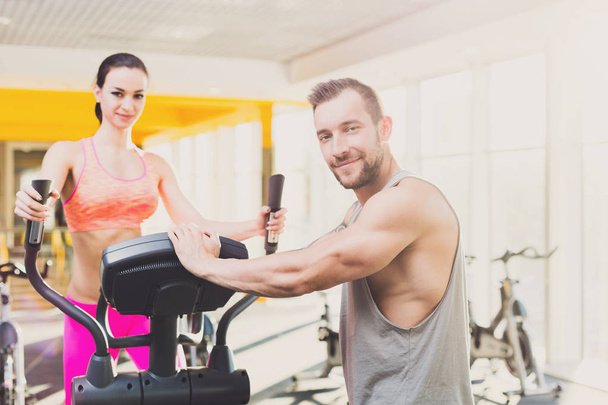 Couple, man helps young woman on elliptical trainer - Photo, Image