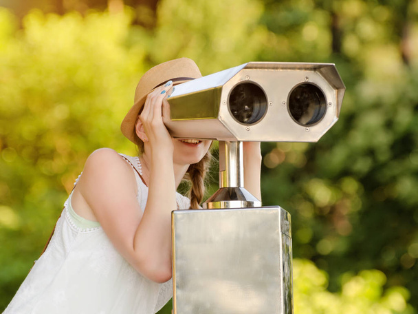 Girl in the hat looks into the big binoculars. Green on the background. Front view - Foto, Bild