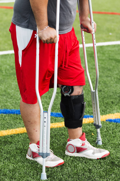 Gewond atleet in een knie brace op krukken - Foto, afbeelding