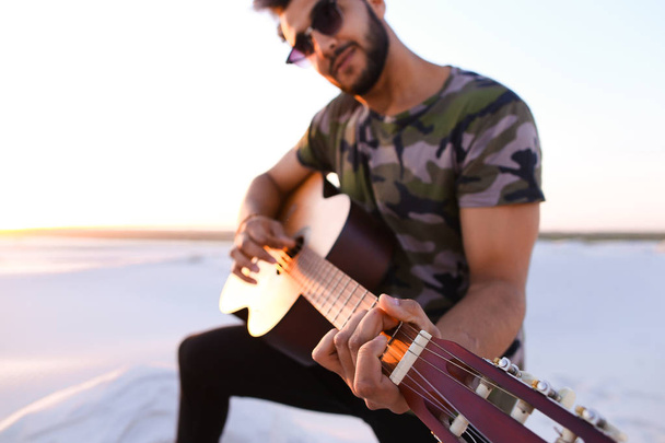 Όμορφος Arabian άντρας παίζει κιθάρα της, στέκεται στο λόφο μεταξύ των άμμου - Φωτογραφία, εικόνα