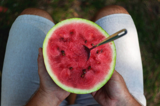 A young man is eating a watermelon with a spoon. The concept of  - Zdjęcie, obraz