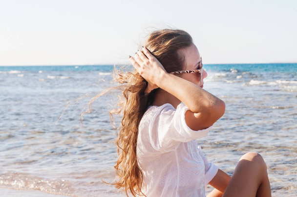 Una joven con gafas de sol sostiene una mano sobre su cabello revoloteando
  - Foto, Imagen