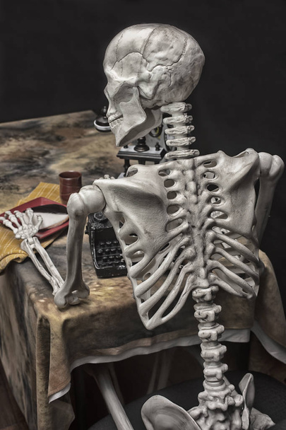 Esqueleto de Halloween en una mesa con máquina de escribir, teléfono y cookies
 - Foto, Imagen