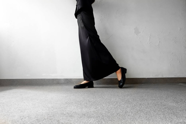 Suru jalat Nainen musta tasainen kengät ja musta mekko seisoo betoni tausta
 - Valokuva, kuva