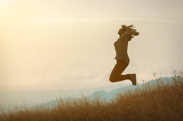 Meisje springen op berg en plezier op idyllische veld op zonnen - Foto, afbeelding