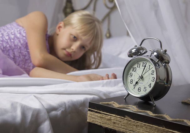 Early awakening. Wake up of an asleep young girl stopping alarm clock on a bed in the morning - Foto, Imagem