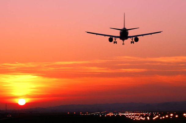 lentokone laskeutuu lentokentälle taustalla punainen auringonlasku
 - Valokuva, kuva