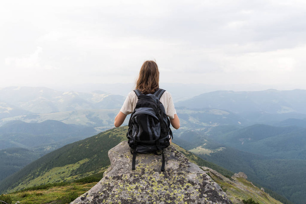 Young woman with tourist rucksack takes rest top of the hill in carpathian mountains and enjoys beautiful scenery - Valokuva, kuva