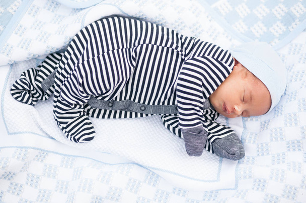 Sleeping newborn baby in striped romper on coverlet. - Photo, Image