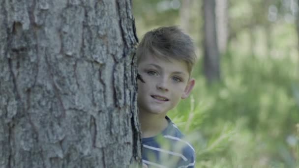 Boy peeking around tree trunk - Filmati, video