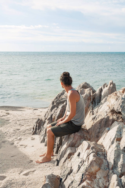 jonge man zittend op het strand en kijk op de horizon lijn - Foto, afbeelding