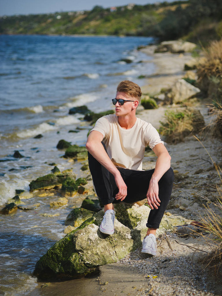 Handsome man sitting near water. A thoughtful guy on a blurred natural background. Male confidence concept. Copy space. - Foto, Imagem