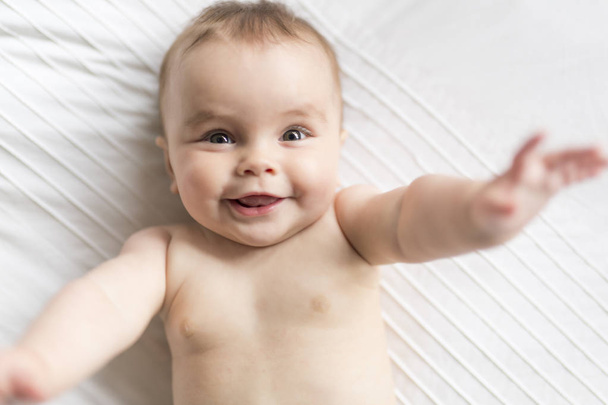 Cute happy 7 month baby girl in diaper lying and playing - Φωτογραφία, εικόνα