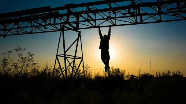 Silhouette of an athlete who pull-ups on a metal frame. Young man doing pull-ups in an abandoned construction site - Footage, Video