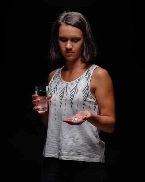 Woman taking medicine. Modern sports girl looking at vitamins in tablets on a black background. Contraception concept. - Foto, immagini