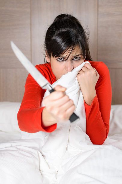 Terrified woman in bed holding knife for self defense - Foto, Imagen