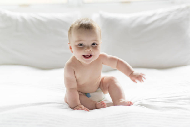 Cute happy 7 month baby girl in diaper lying and playing - Photo, image