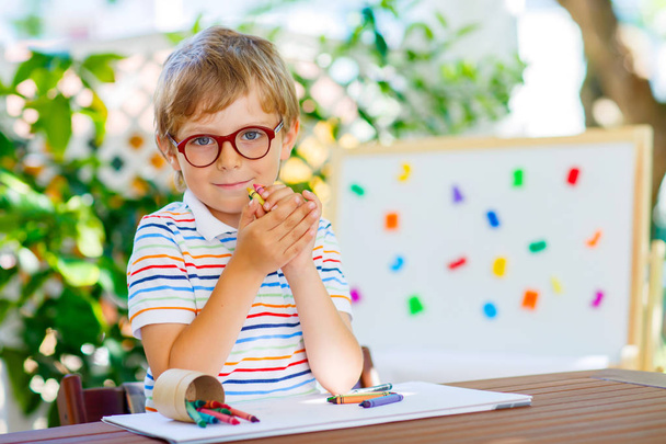 niño de la escuela con gafas que sostienen lápices de cera
 - Foto, imagen