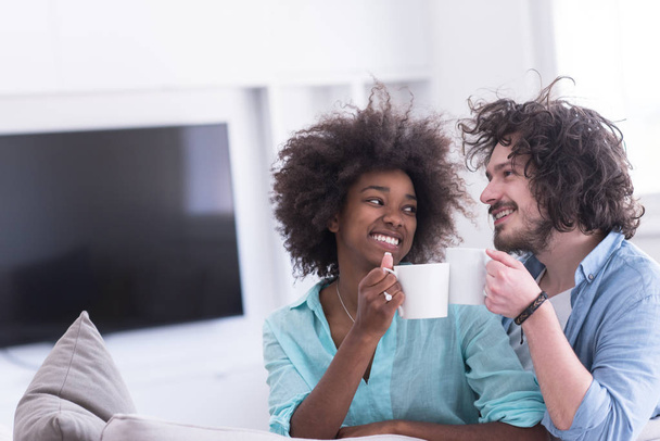 multiethnic couple sitting on sofa at home drinking coffe - Photo, image