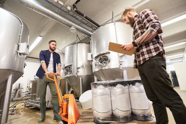 men with beer kegs and clipboard at craft brewery - Foto, afbeelding