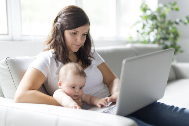 mother and baby child are looking to play and read computer on the couch at home - Фото, зображення