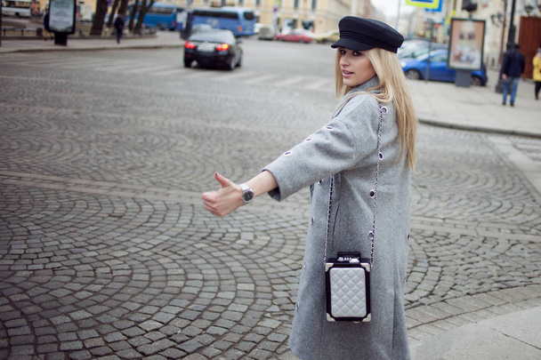Young, hip and attractive blonde hailing taxi , girl in a stylish hat and a gray coat - Foto, immagini